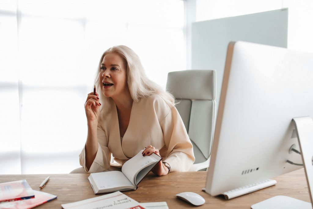 A professional woman engaged in work at a modern office desk with a computer and open books.